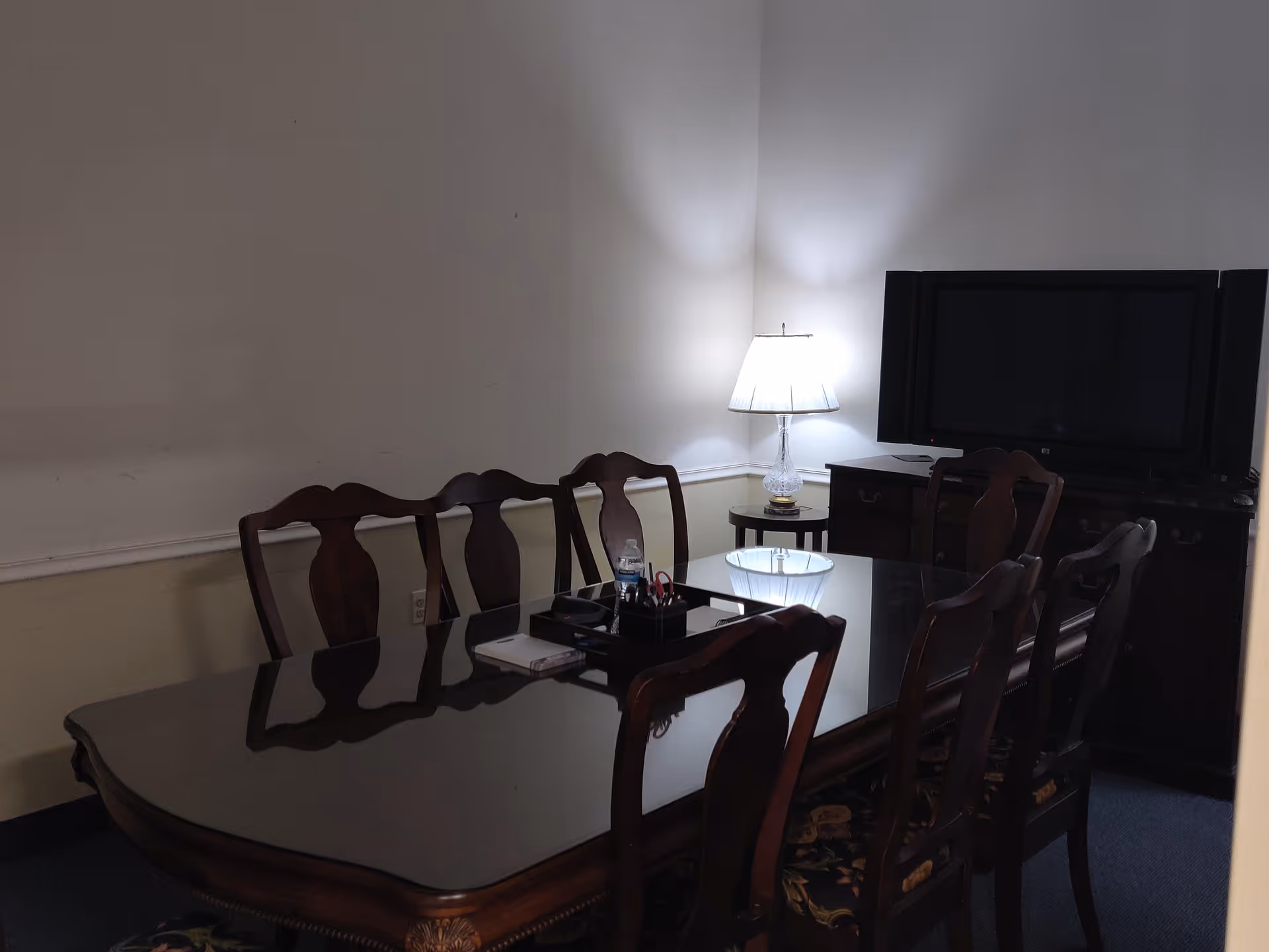 A dark wooden dining table with chairs in a dimly lit room and a TV cabinet.