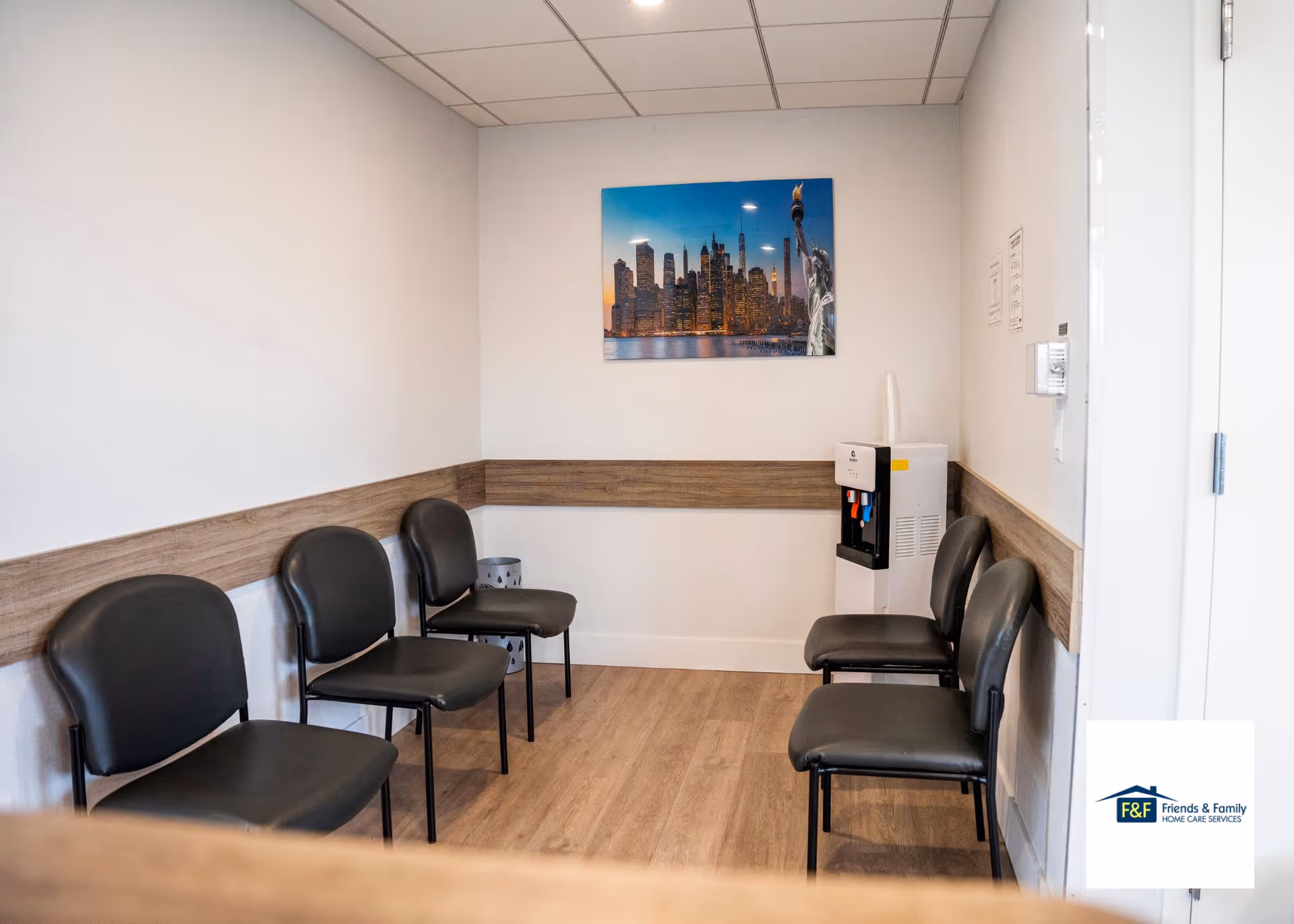 Row of black chairs along walls in a waiting area, with water cooler and skyline art.