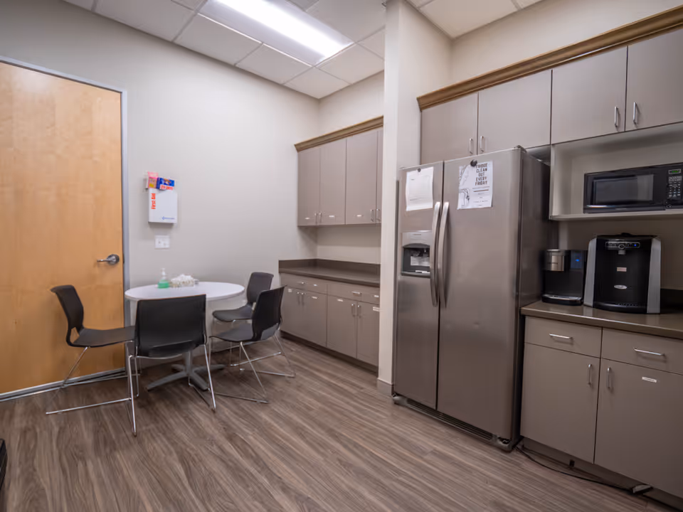A small staff break room with table, chairs, cabinets, fridge, and microwave.