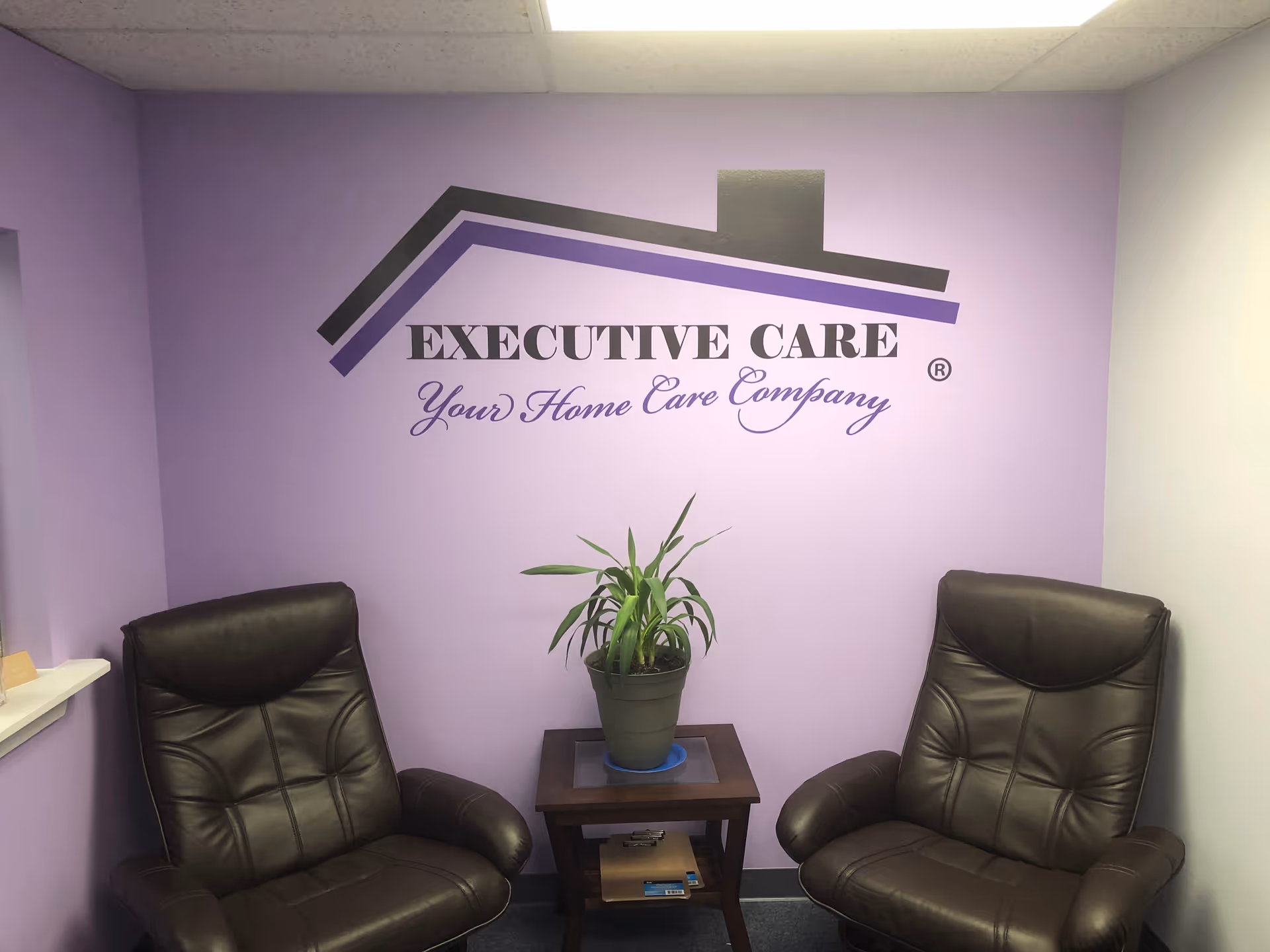 Purple-walled reception area with two leather chairs, a plant, and Executive Care logo.