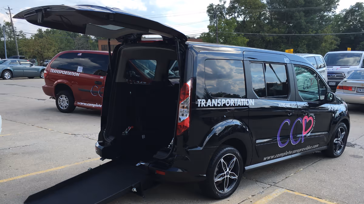 Black transportation van with wheelchair ramp extended in a parking lot.