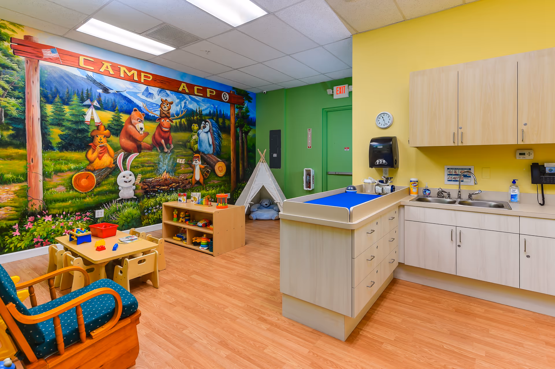 Colorful children's activity room with mural, toys, a small table, and a kitchenette.