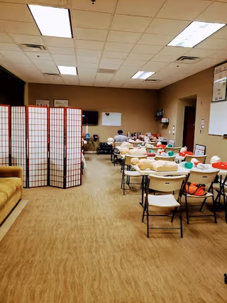 Indoor training room with tables, chairs, partition screens, and people attending CPR class.