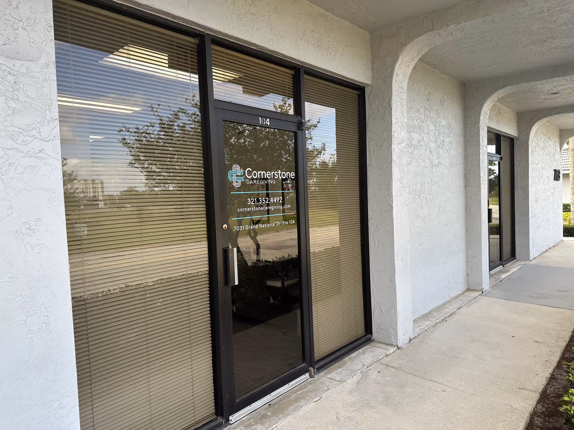Exterior building entrance with glass doors, blinds, and Cornerstone Caregiving logo.