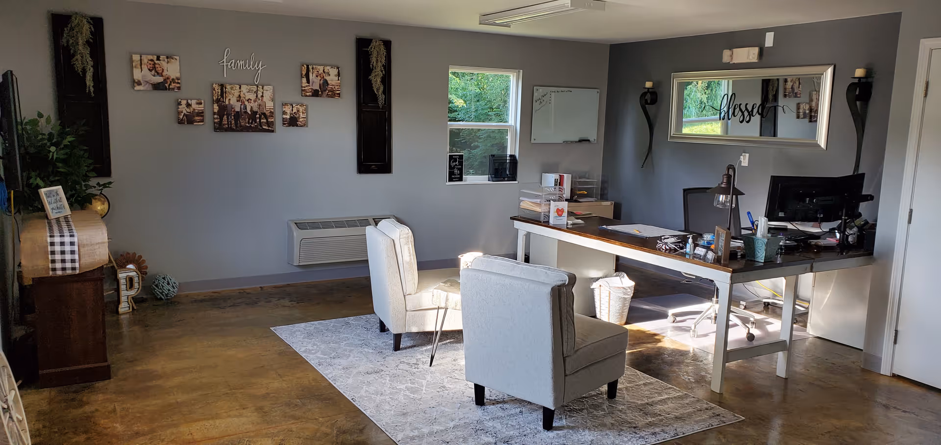 Modern reception lounge area with two beige chairs, a desk, wall photos, and window light.