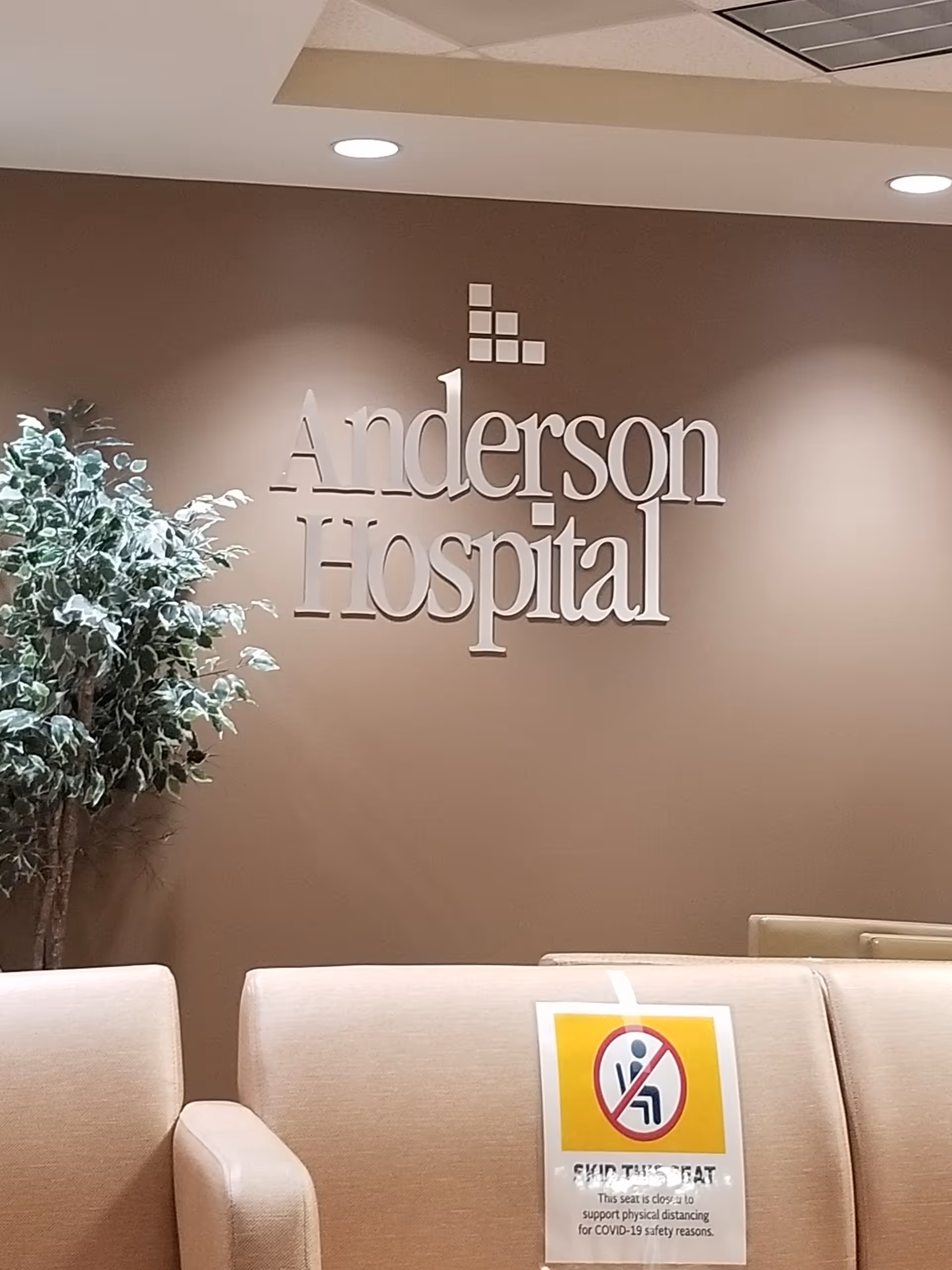 Indoor hospital lobby with Anderson Hospital sign, beige seating, and a safety sign.