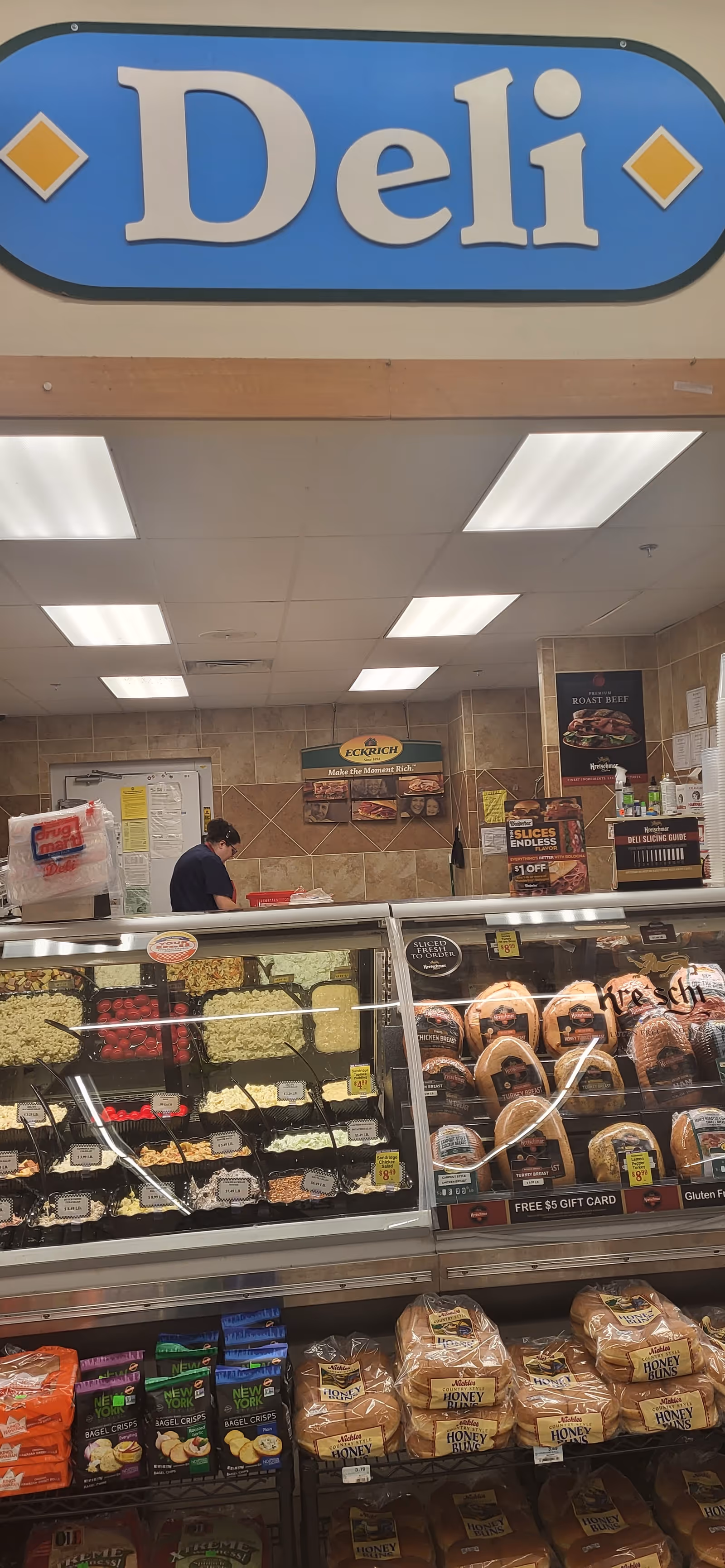 Inside Discount Drug Mart deli: glass display case with meats and breads beneath a Deli sign.