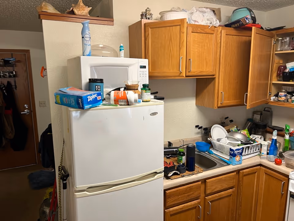 Cluttered kitchen in a BrightStar Care facility with fridge, microwave, and dishes.