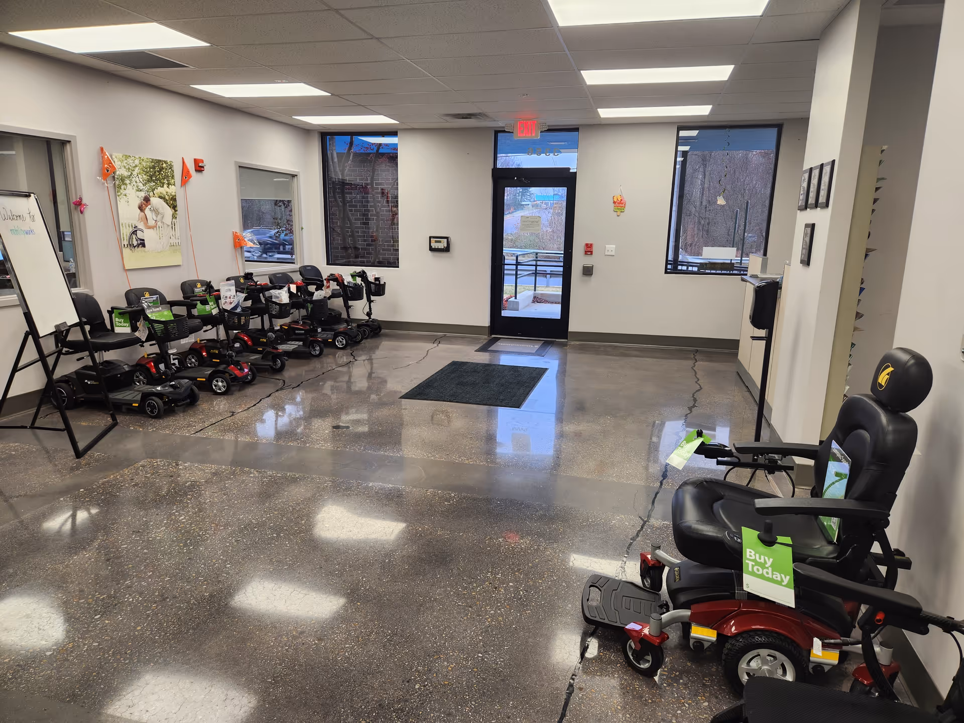 A showroom-like interior with mobility scooters lined along the left wall and chairs on the right.