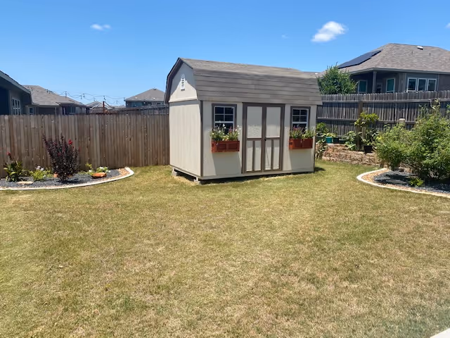 Backyard with a small shed, lawn, and circular garden beds in a fenced yard