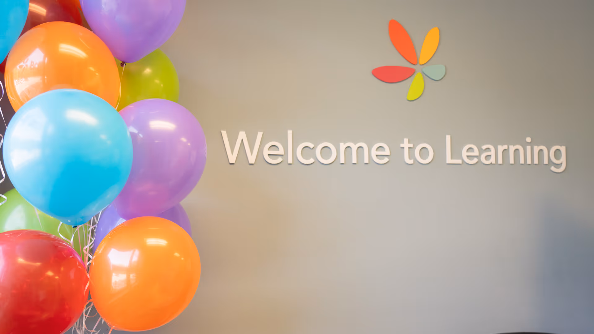 Colorful balloons frame a wall with 'Welcome to Learning' in a bright indoor space.