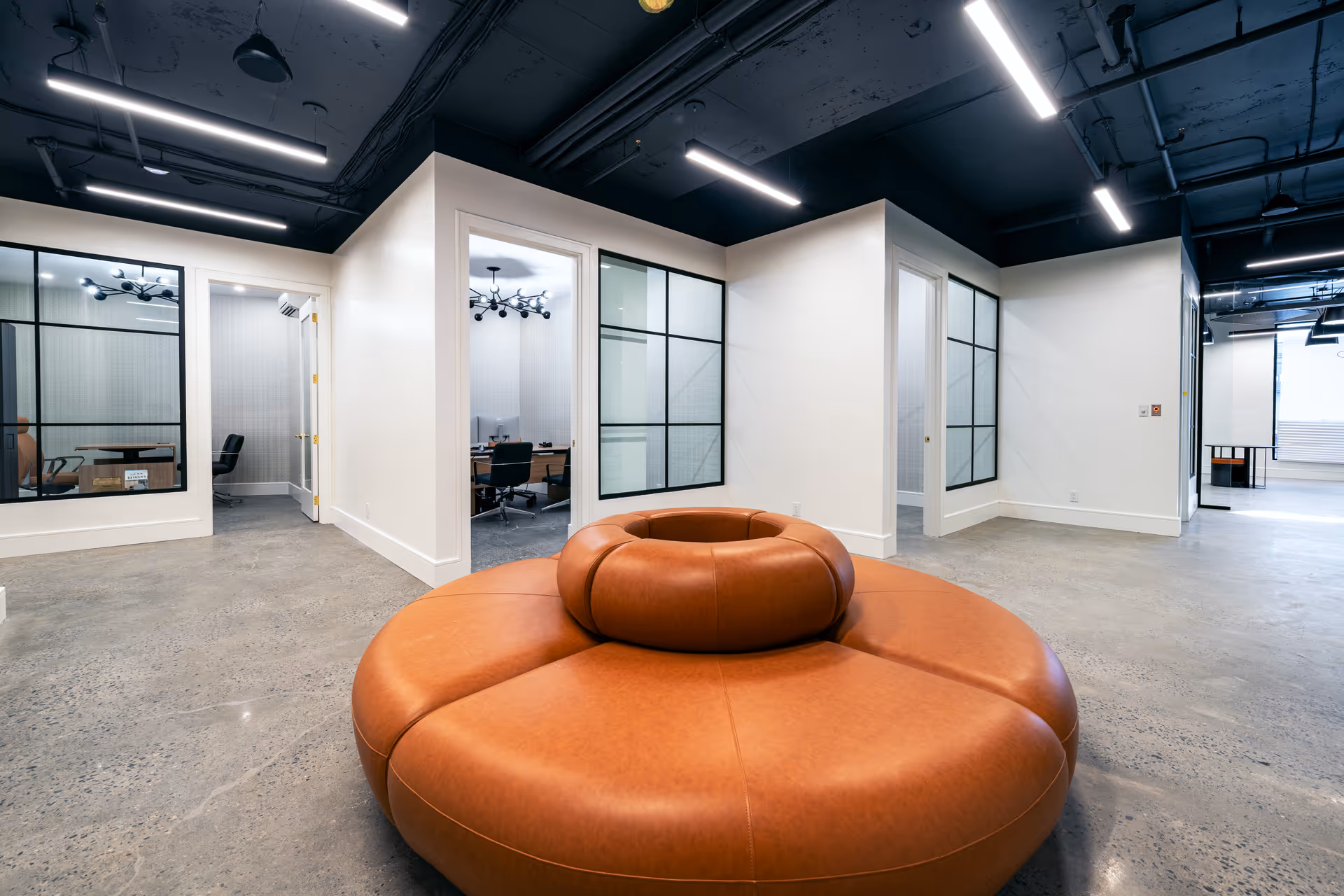 Open modern lounge area with circular orange seating, glass-walled offices, and polished concrete floor.