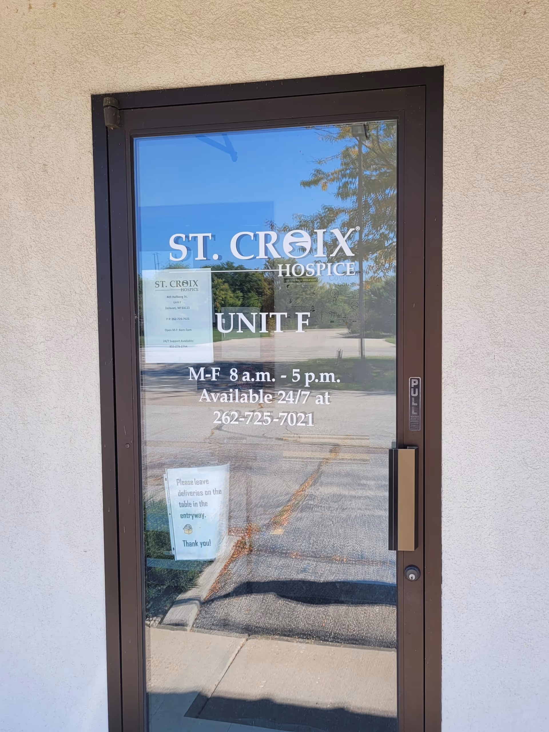 Glass entrance door labeled ST. CROIX HOSPICE Unit F, reflecting outdoor surroundings.