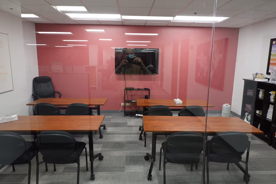 Conference room in a senior care facility with pink glass wall, TV, and arranged tables.