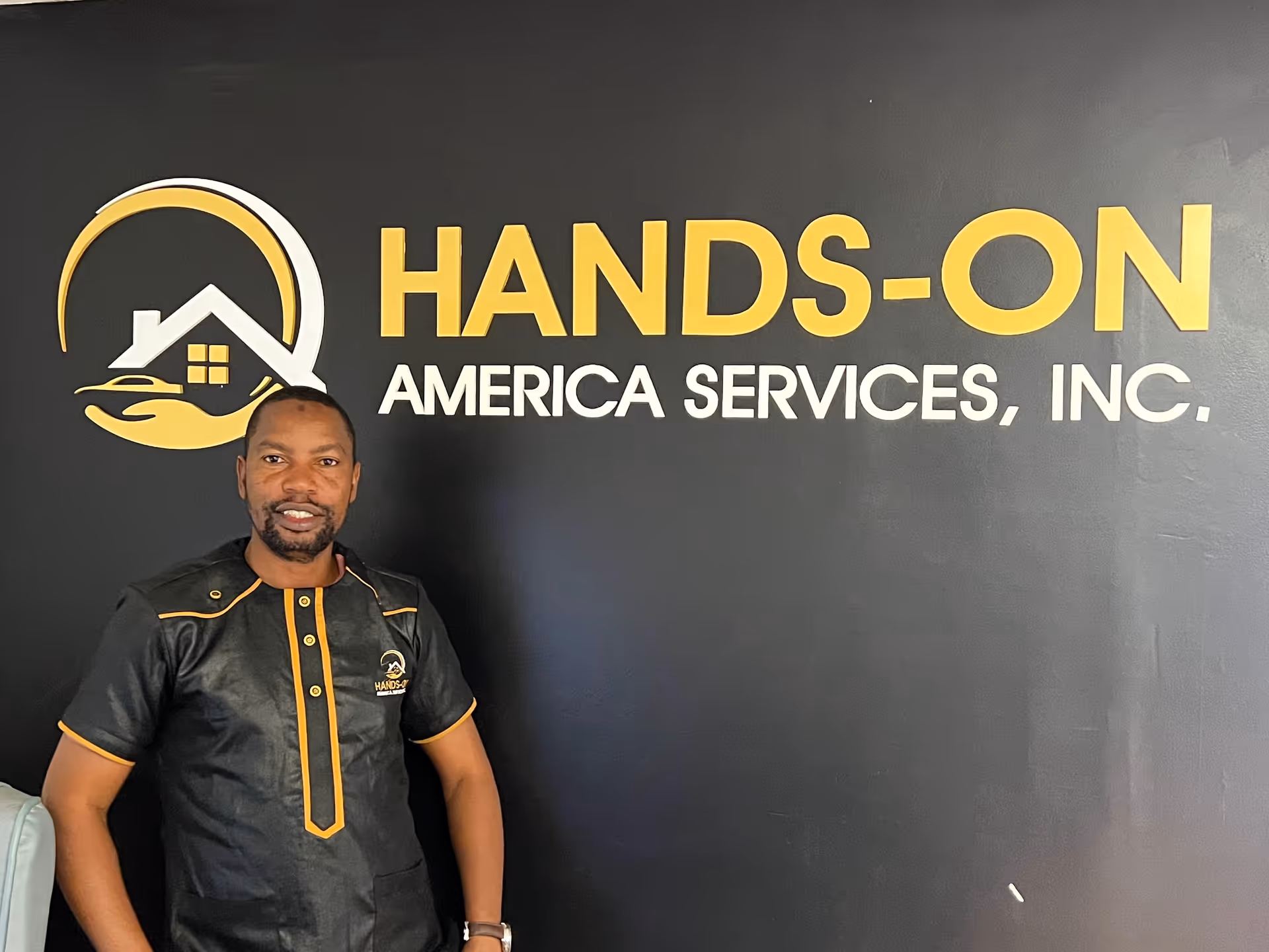 Staff member in uniform stands beside a large Hands-On America Services wall logo.