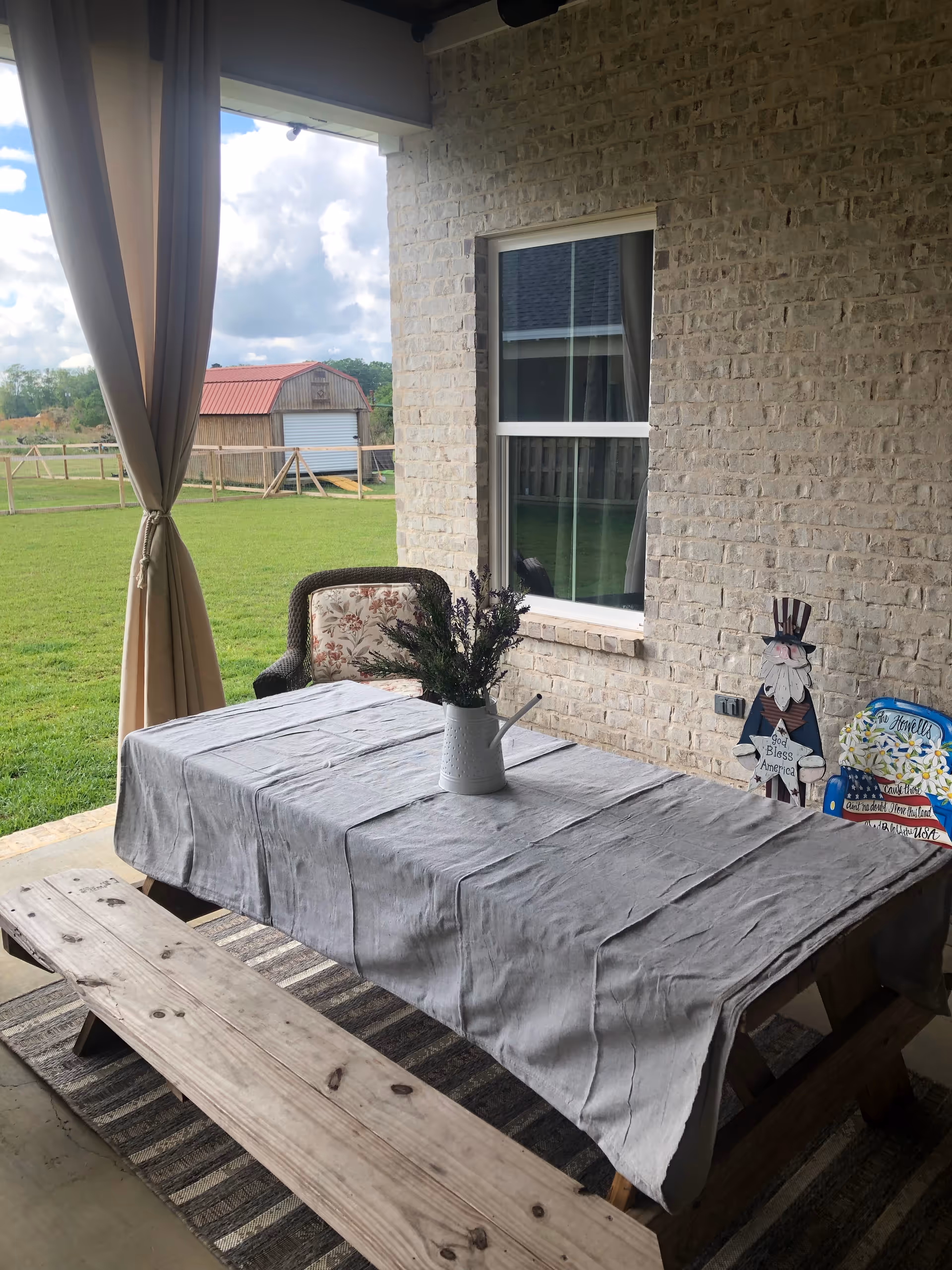 Covered outdoor patio with a table, bench, and potted flowers beside a brick wall.