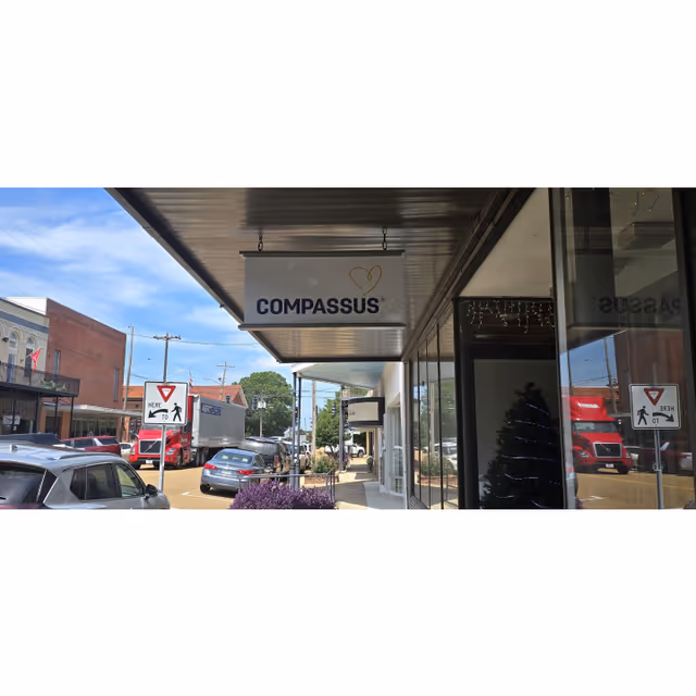Exterior view of a Compassus facility storefront with a hanging sign and street traffic.