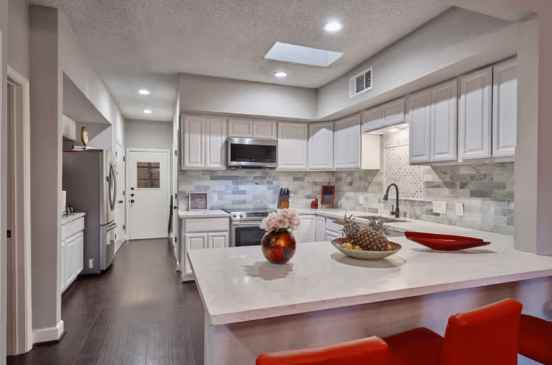 Bright modern kitchen with island, grey tile backsplash, and stainless appliances.