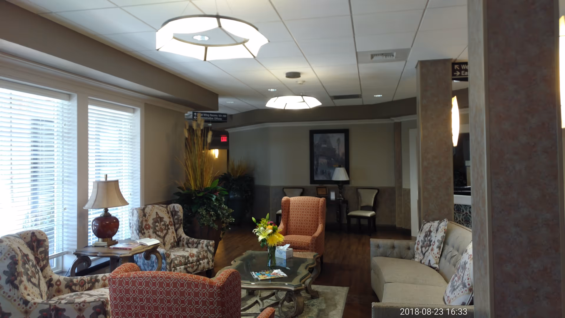 A cozy lounge in a senior living facility with sofas, chairs, coffee table, lamps, and plants.
