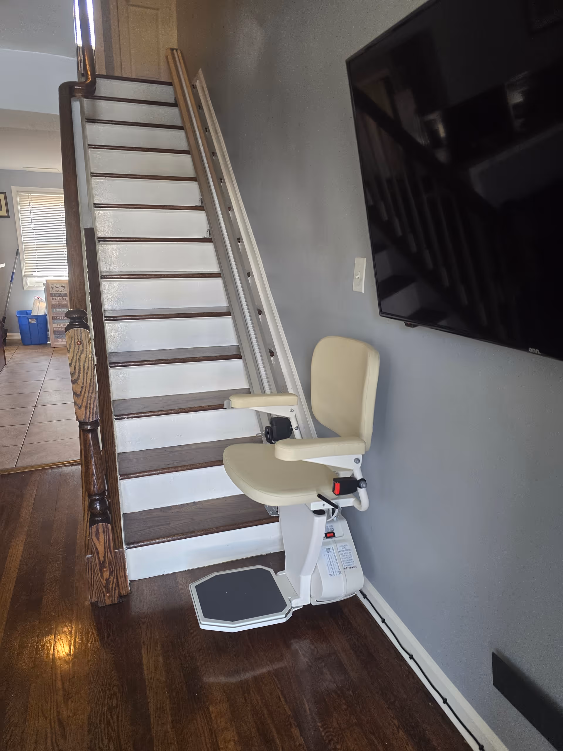 Inside living area with a stairlift chair attached to a wooden staircase beside a wall.