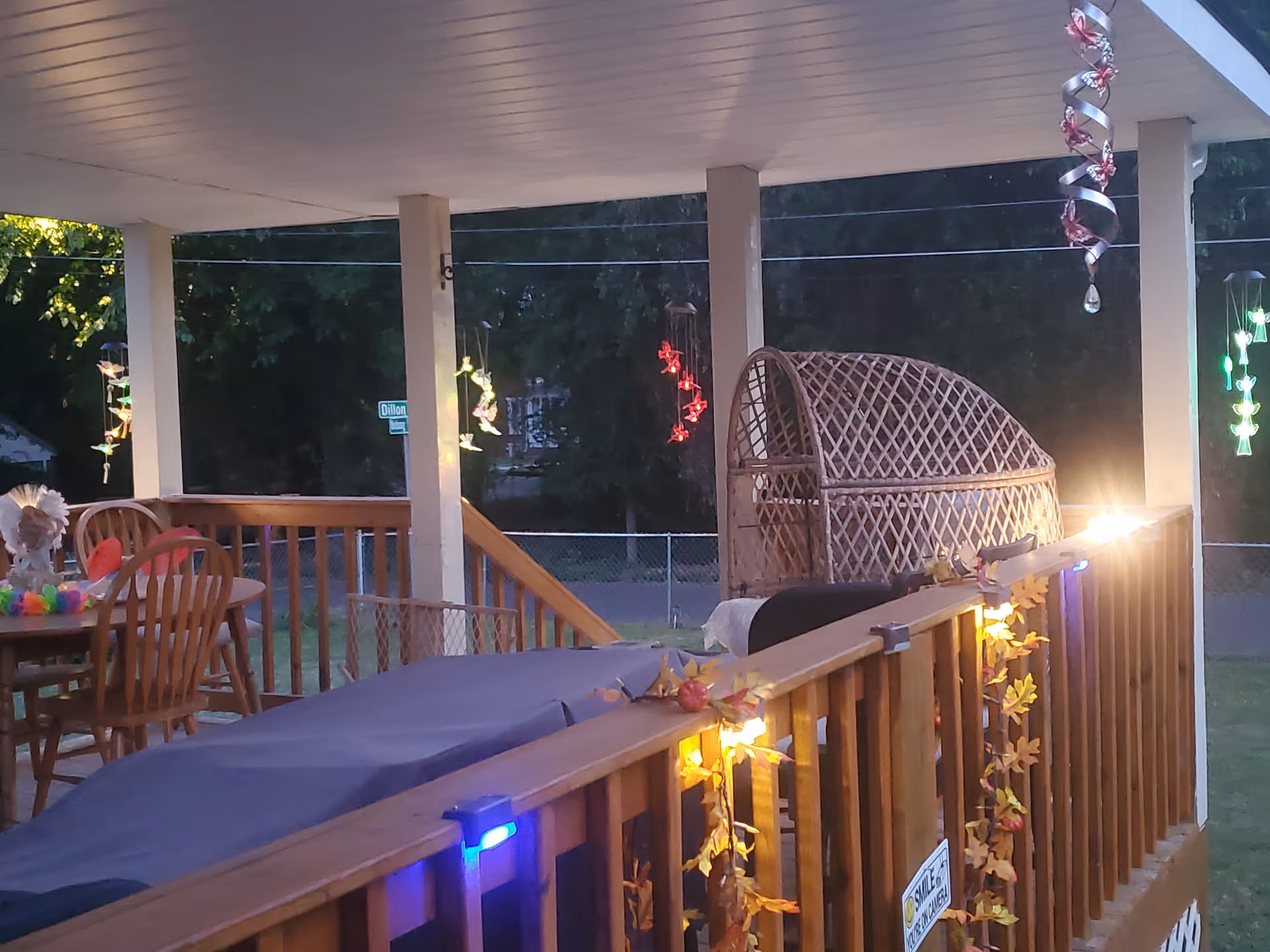 Outdoor covered porch with tables, chairs, and decorative string lights on railing.
