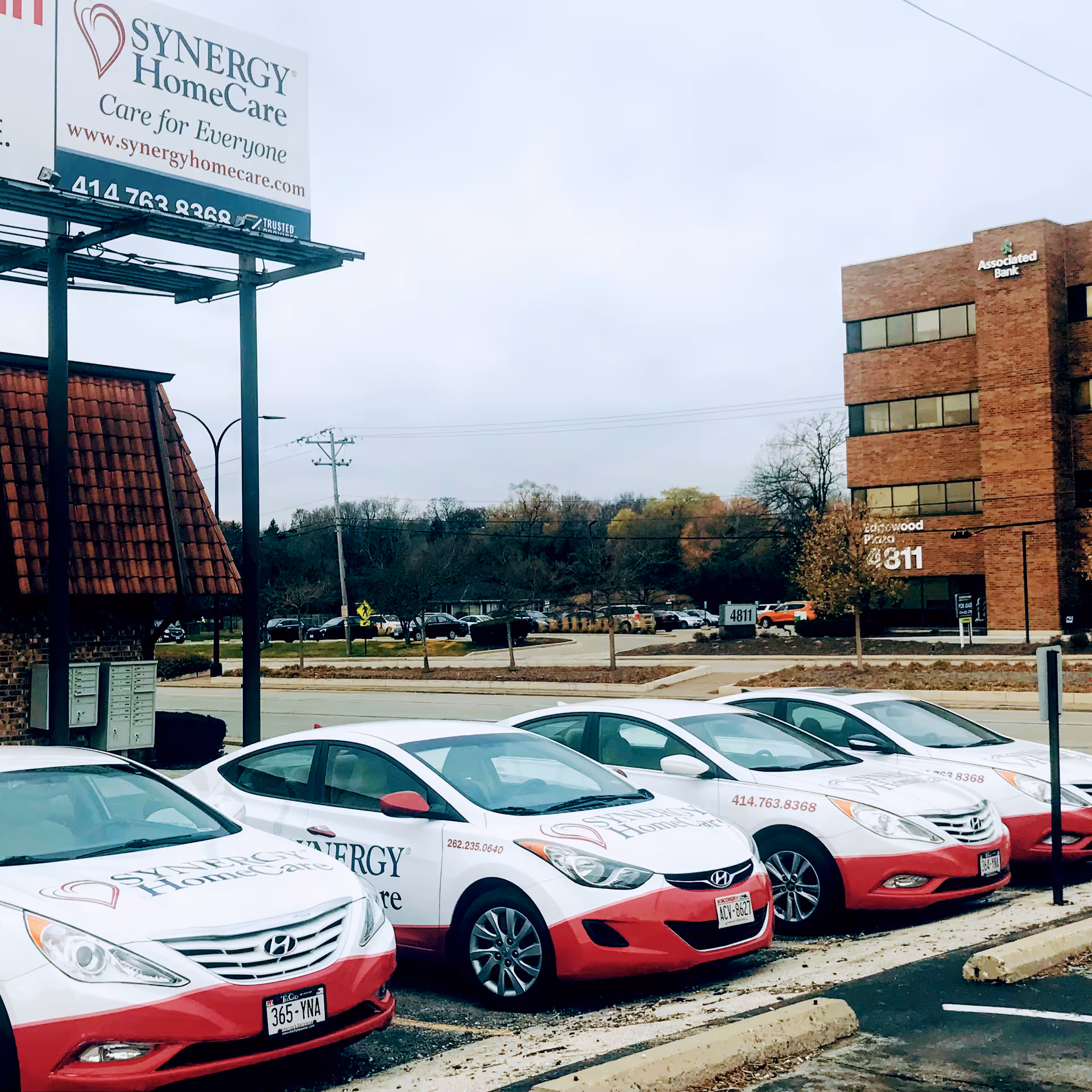Exterior street view of Synergy HomeCare billboard and branded cars in parking lot.