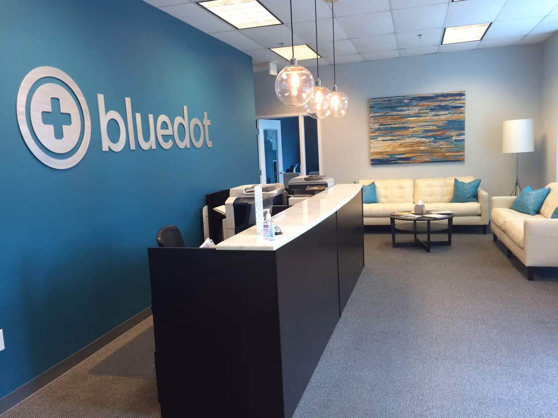 BlueDot Cares reception area with teal wall, logo, and white seating.