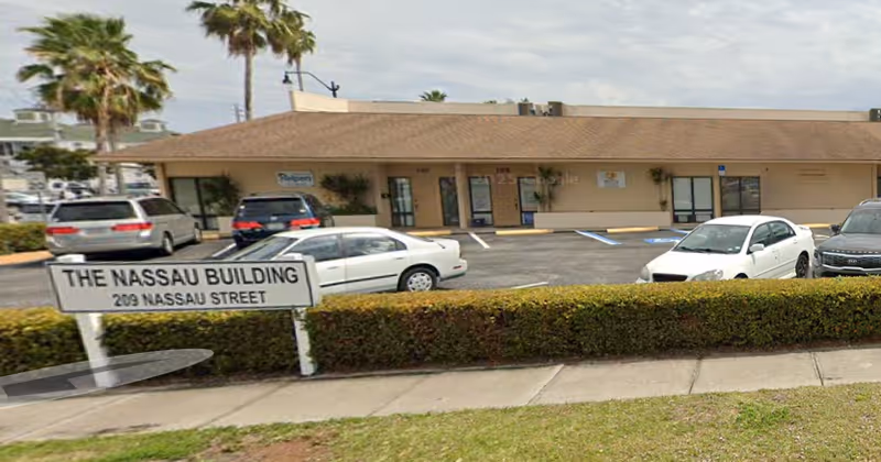 Exterior view of The Nassau Building with parked cars and palm trees.