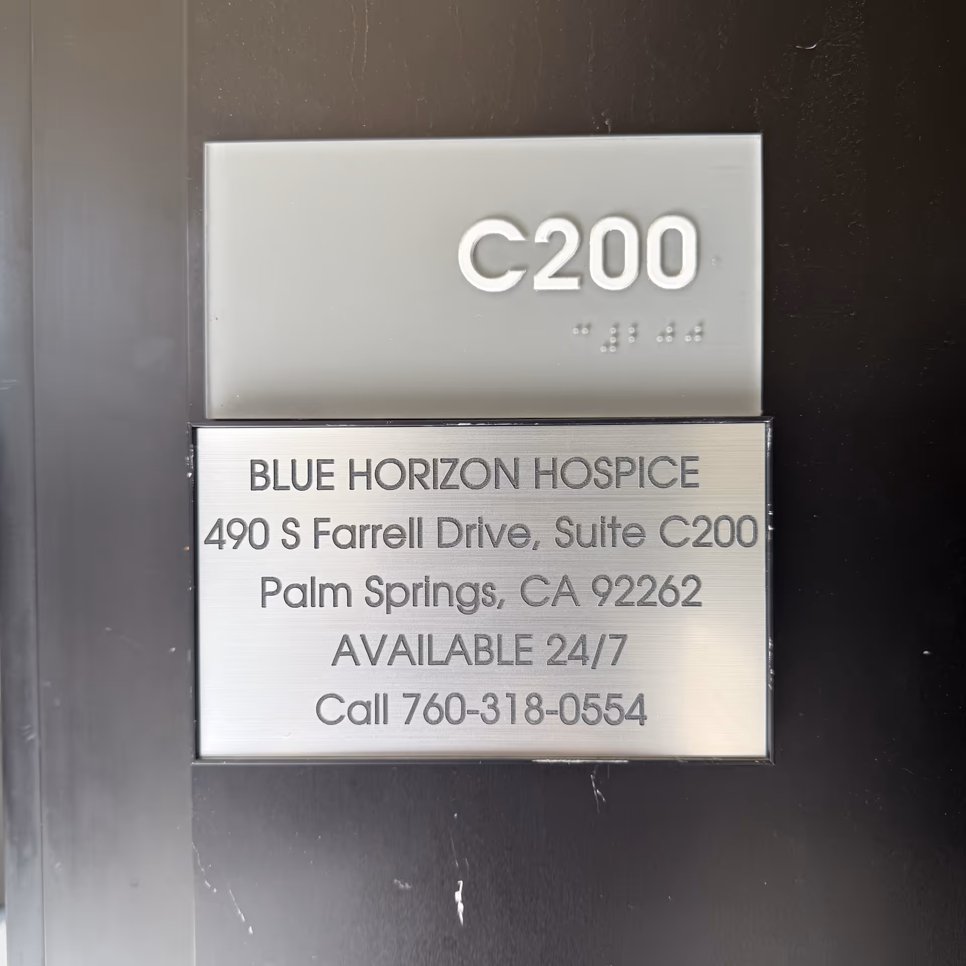 Metal plaque on a dark wall shows Blue Horizon Hospice C200 address and contact.