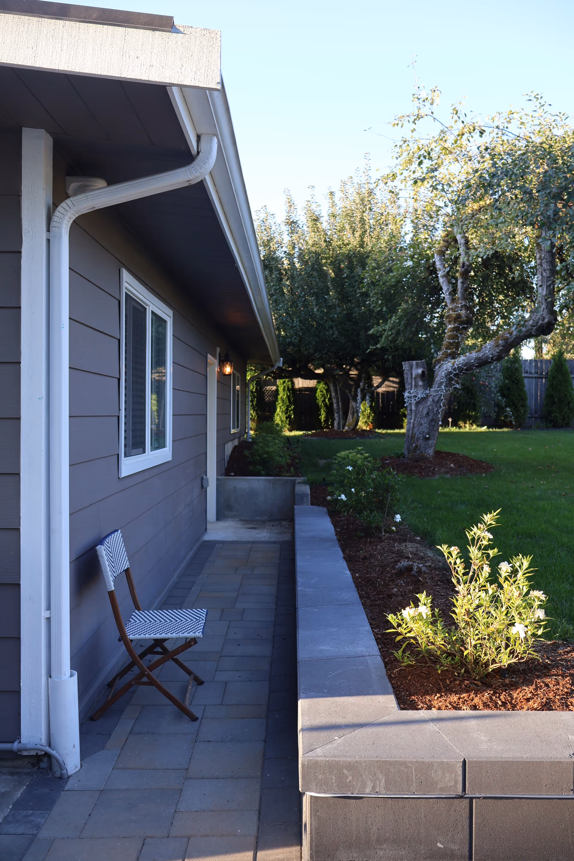 Outdoor patio along a single-story building with a striped chair and garden beds.