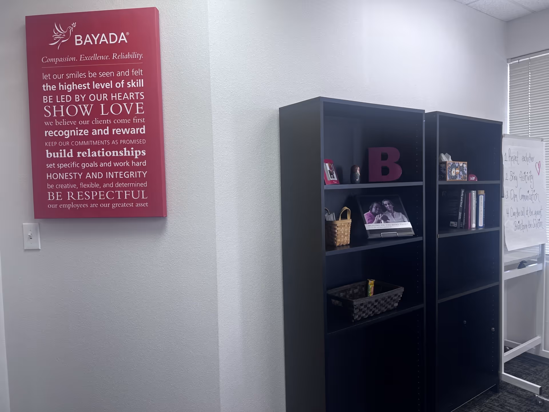 Interior office space with BAYADA poster and two dark bookcases along wall.