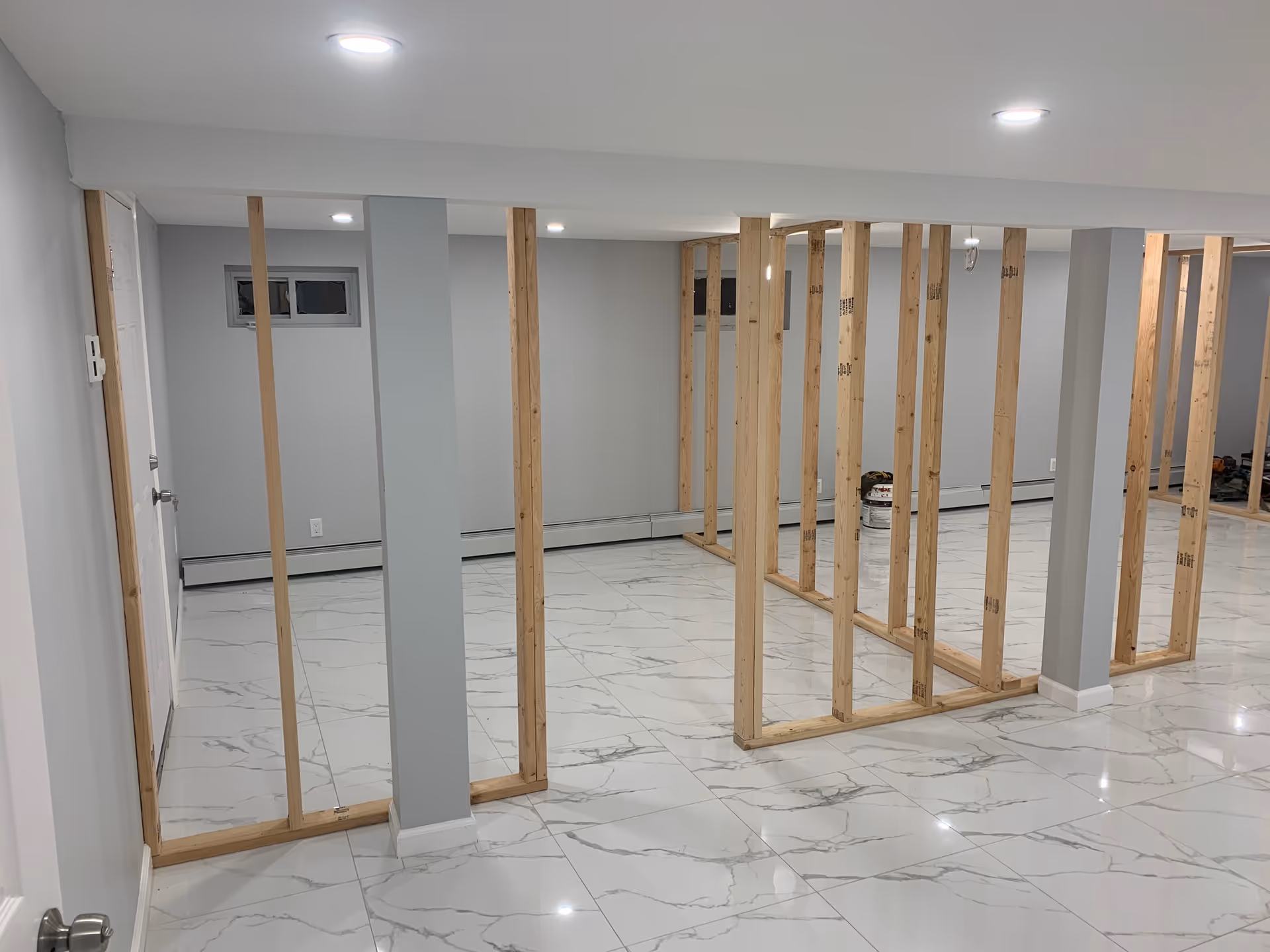 An interior under construction with wooden studs forming partitions in a bright tiled space.