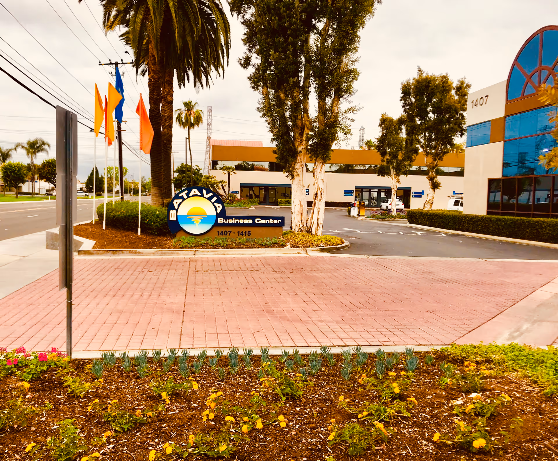 Exterior view of a business center with sign, parking lot, and palm trees.