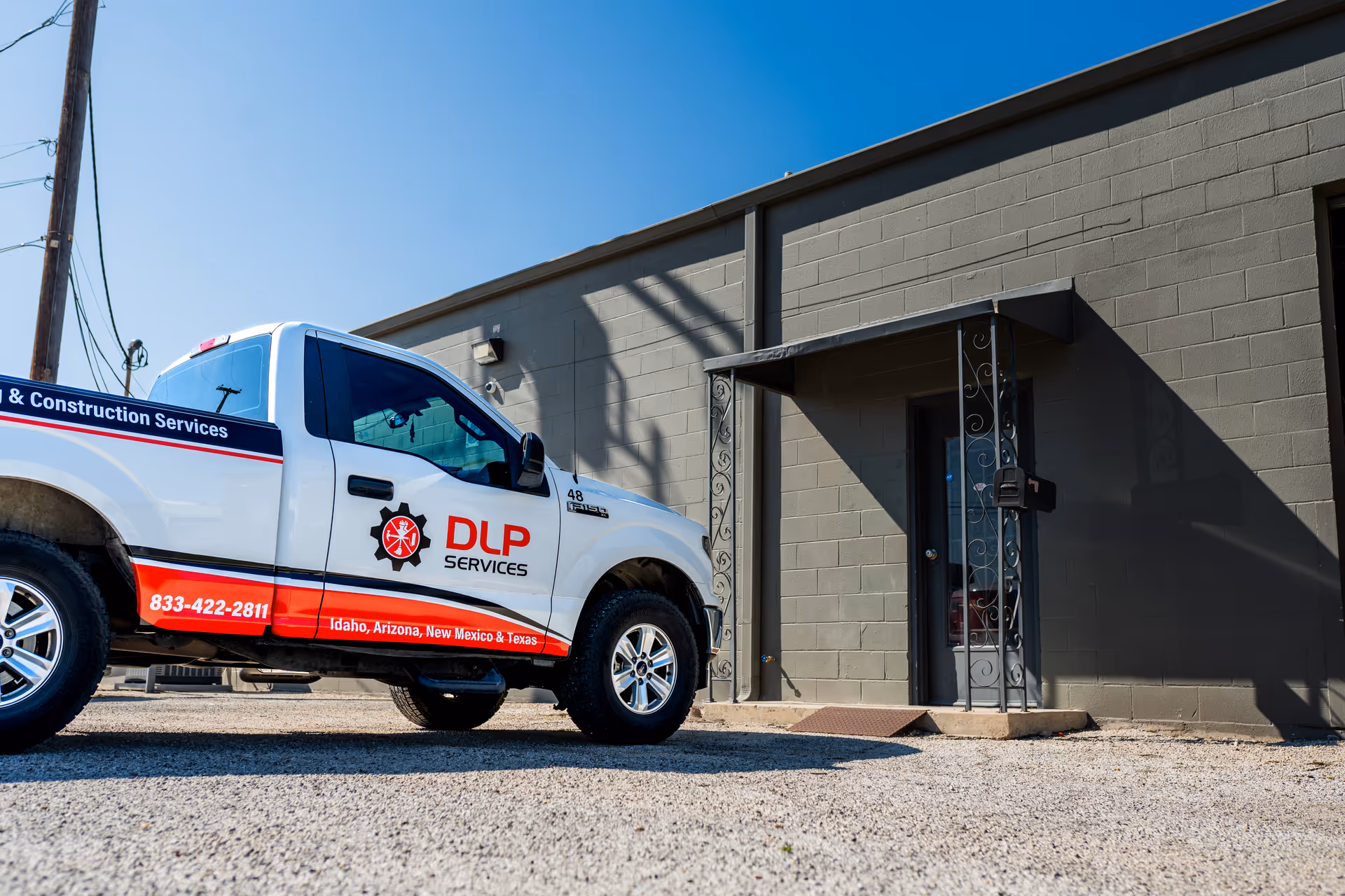 White DLP Services truck parked beside a gray building entrance under clear blue sky
