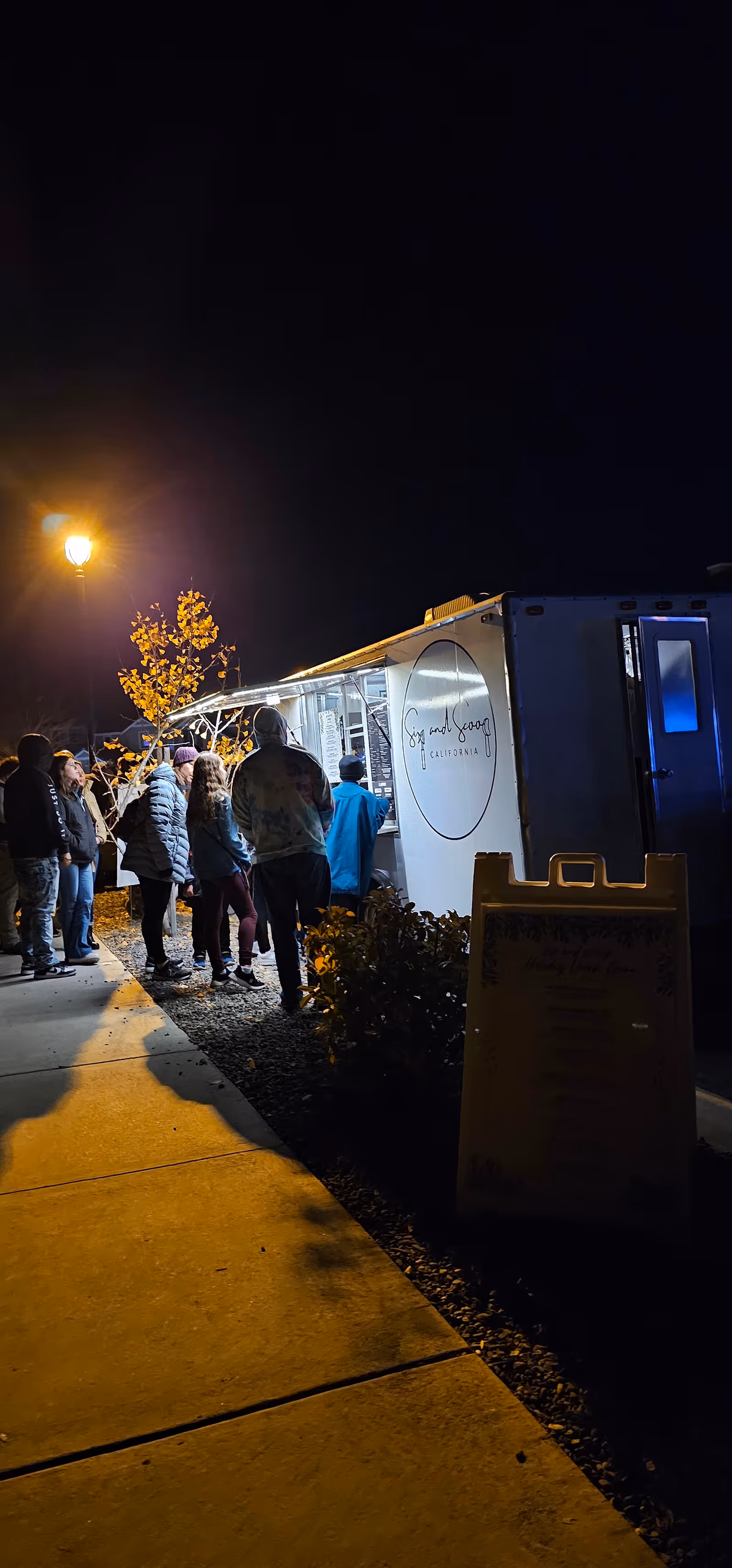 Nighttime outdoor scene with people lined up beside a mobile care unit at a care facility.