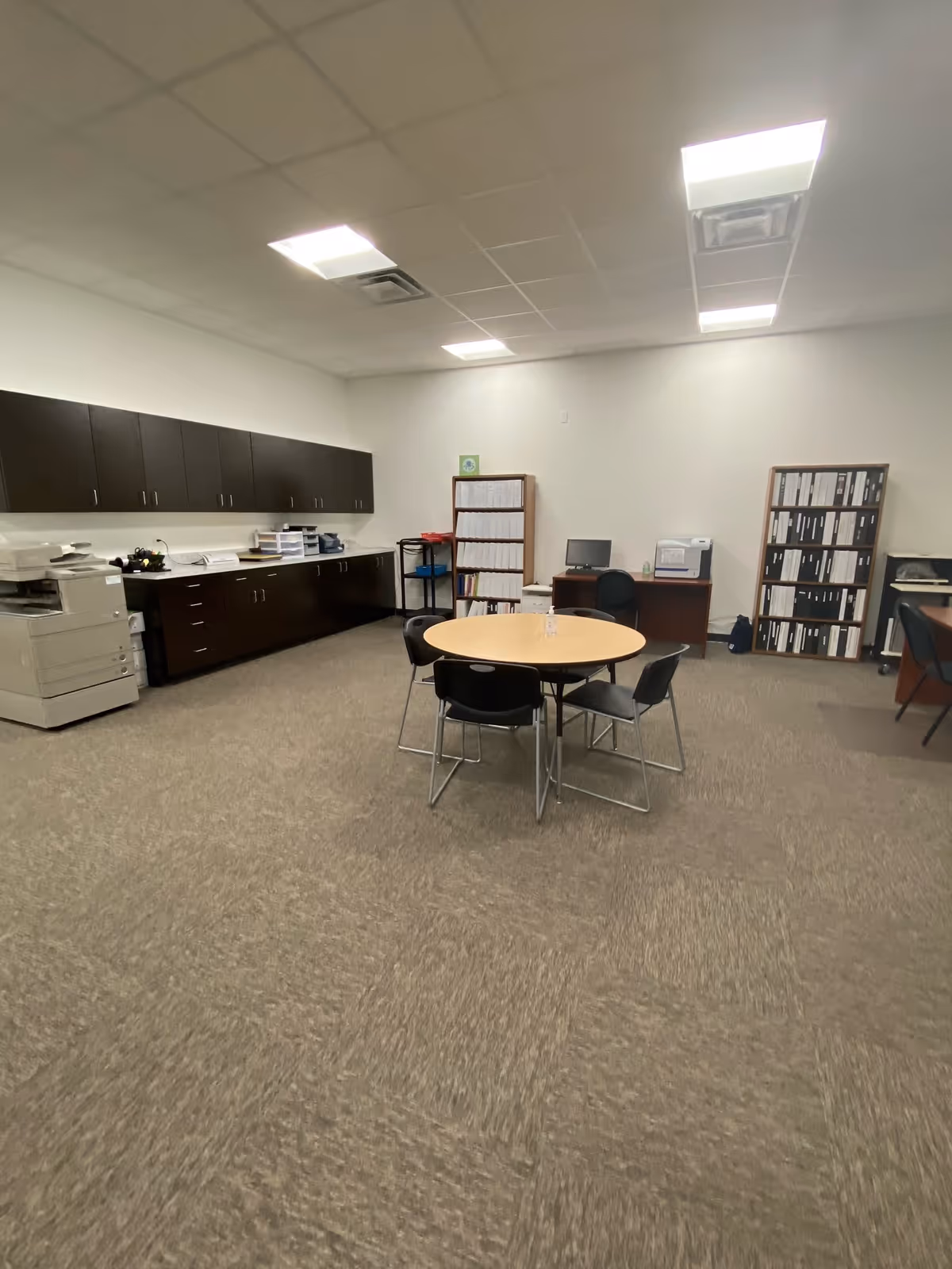 Interior office space with round table, black chairs, cabinets, and shelving.
