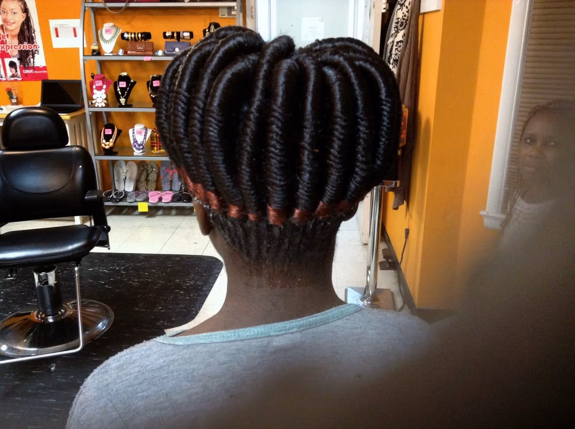 Back of a person with braided hair in a salon, shelves visible behind.