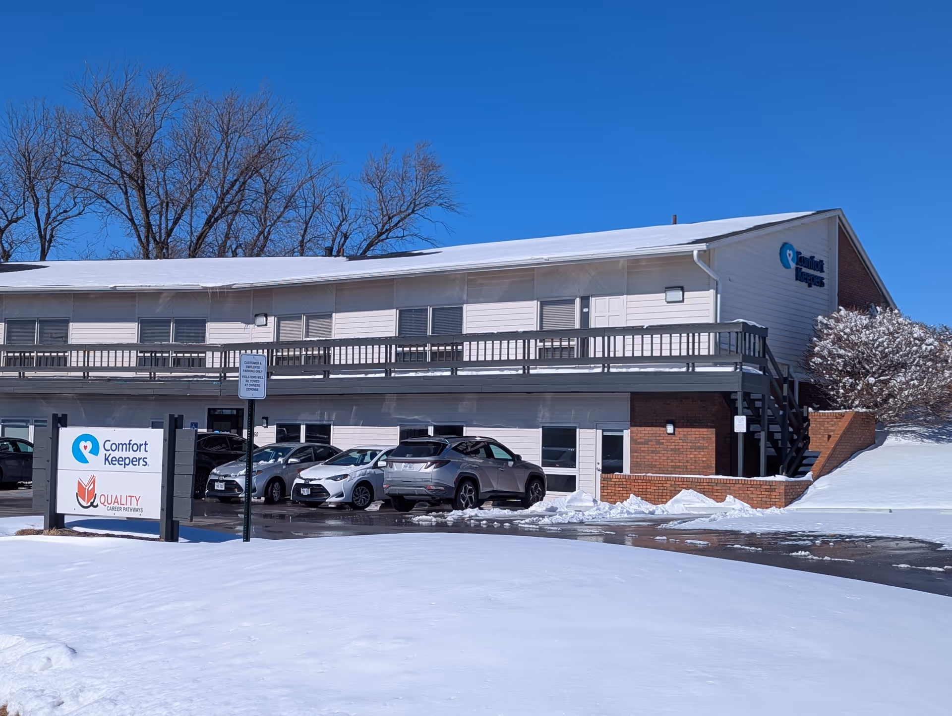 Exterior view of a Comfort Keepers building with snow, parking lot, and vehicles