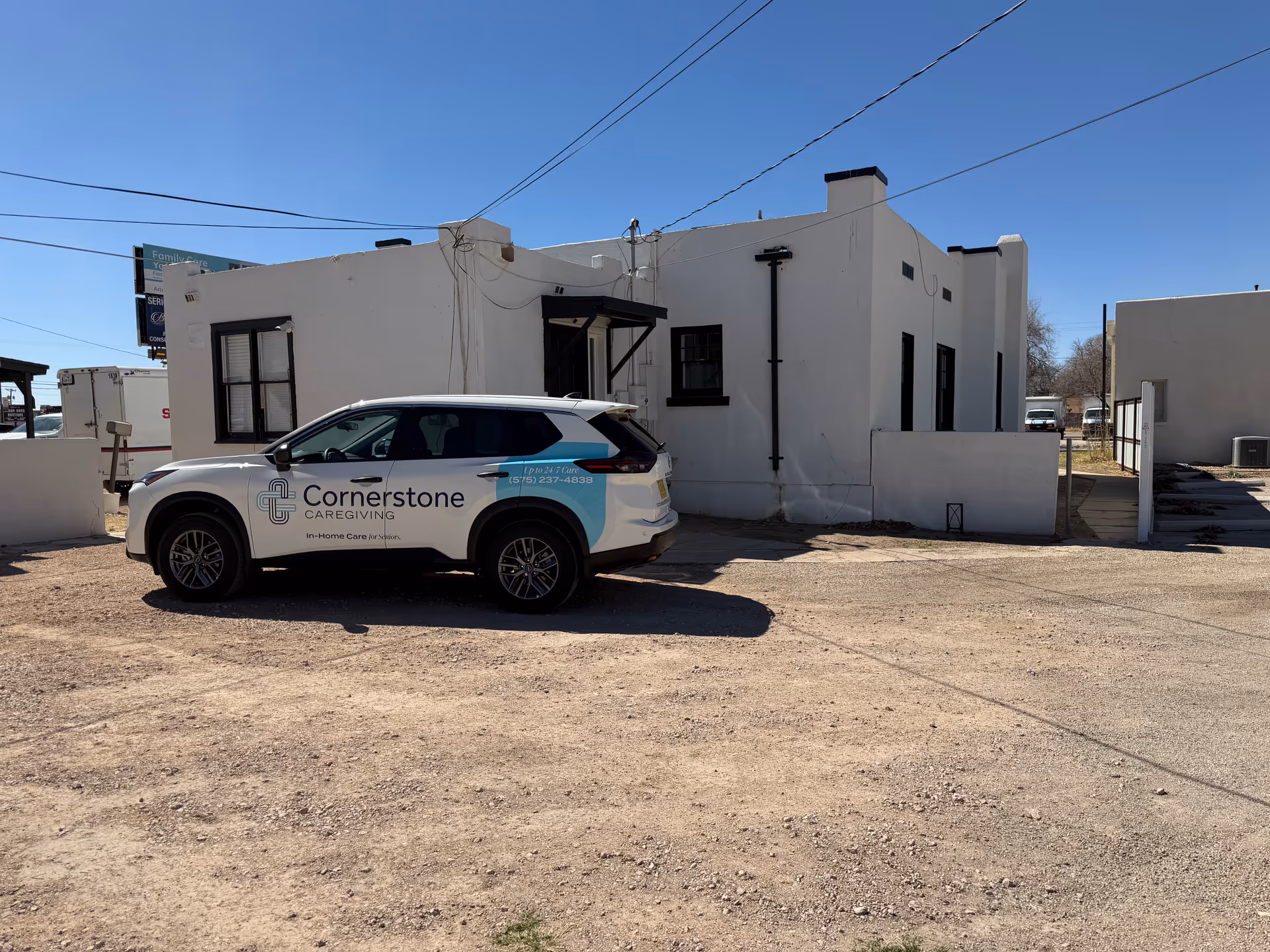 White single-story building exterior with a Cornerstone Caregiving vehicle parked in front.