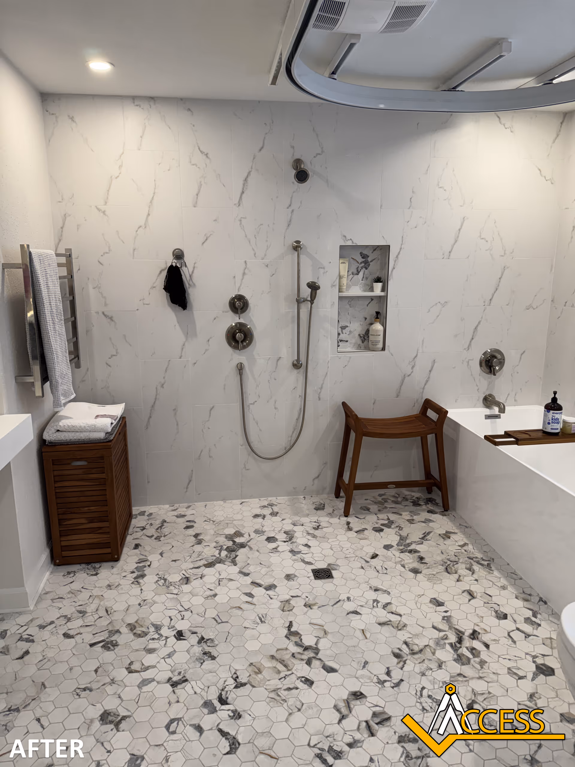 Modern marble-tiled bathroom with accessible shower, wooden bench, and built-in niches; ceiling lift track overhead.