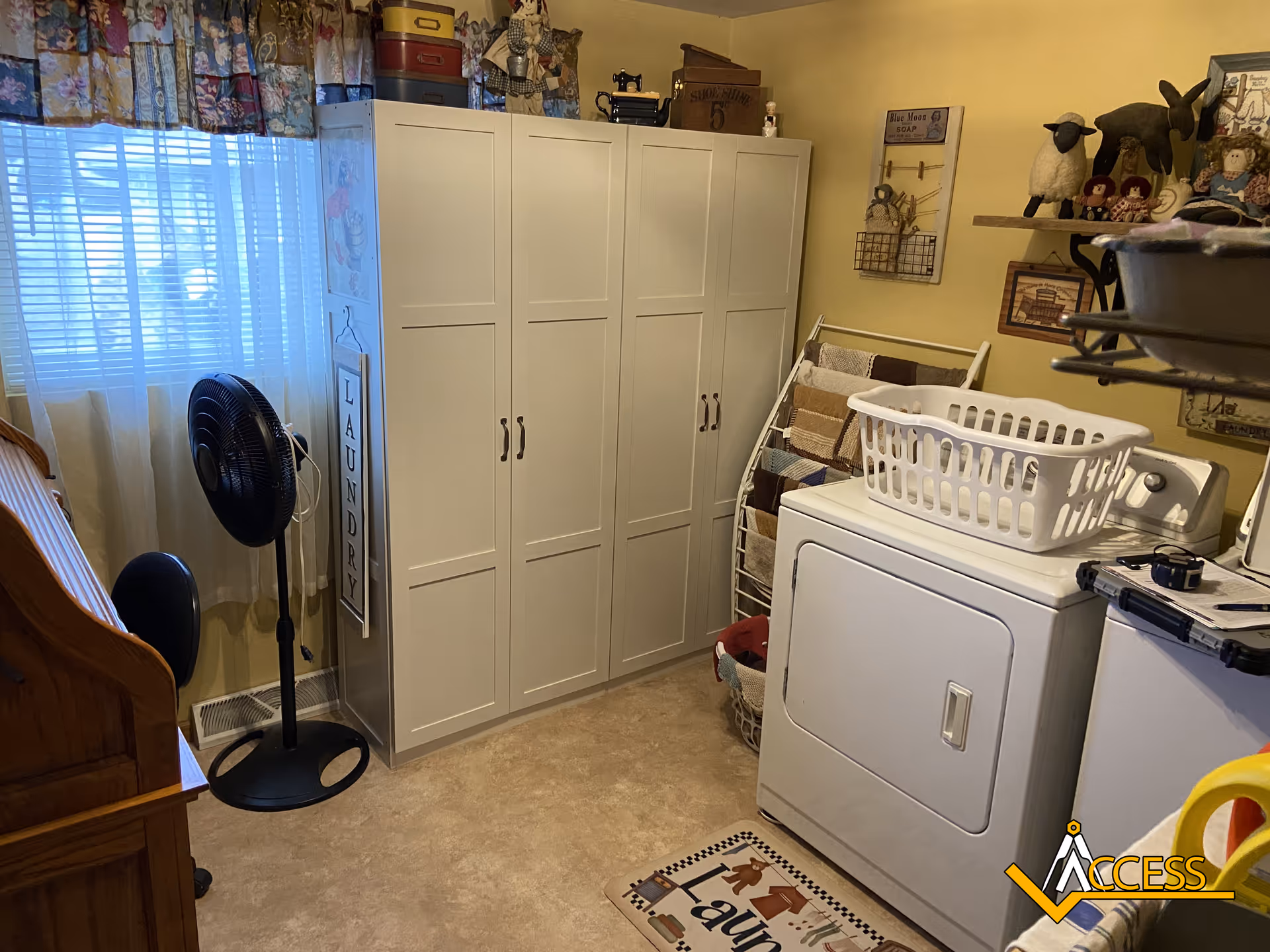 Laundry room with white storage cabinets, washer, dryer, laundry basket, fan, and ironing board.