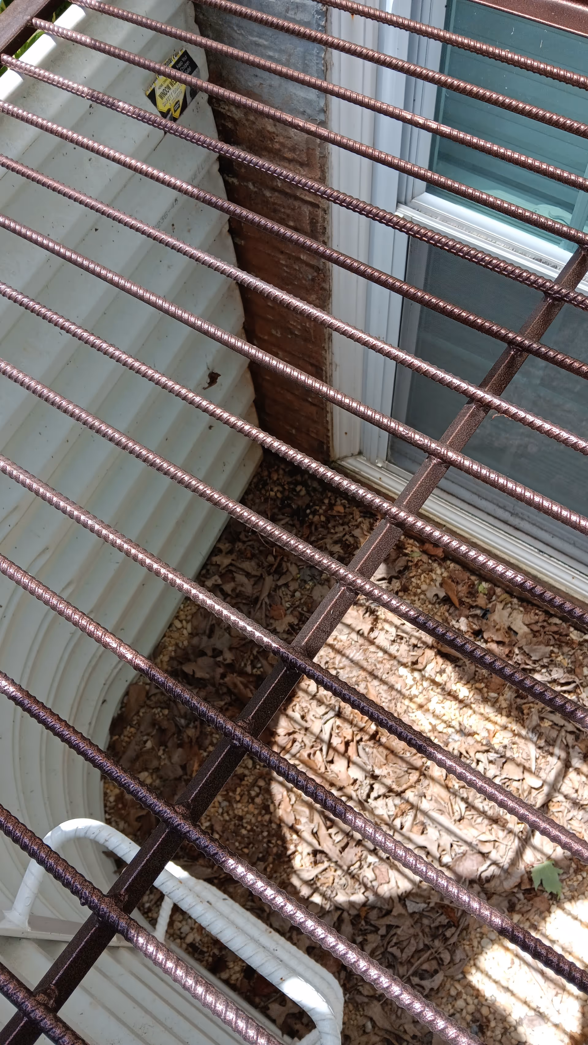 Metal railing across a narrow outdoor space with leaves, brick wall, and a window.