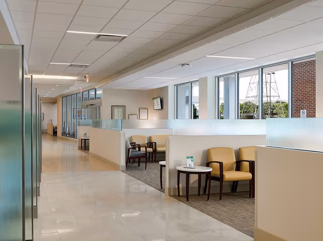 Bright modern clinic waiting area with beige chairs, glass partitions, and a long hallway.