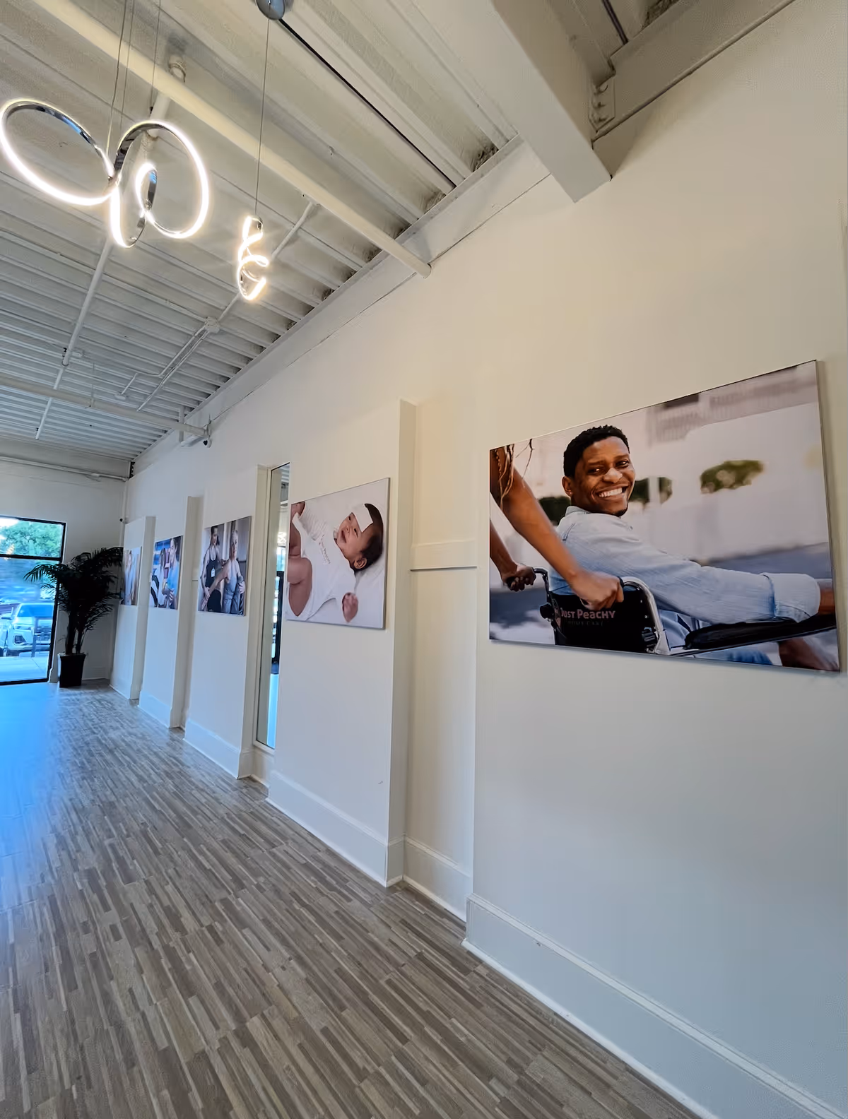 Bright interior corridor with artwork along white walls and wood-look flooring.