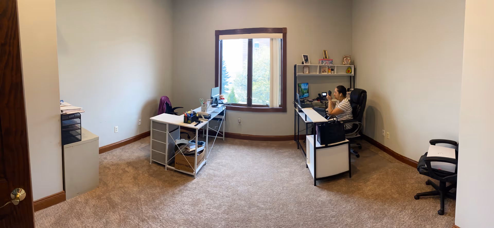 Office-like senior care workspace with desks, a window, and a staff member using a computer.