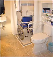 Wheelchair-accessible bathroom with a blue shower chair, grab bars, toilet, and storage shelves.