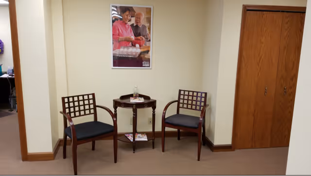 Two wooden lattice-backed chairs flank a round table in a small beige hallway lounge.