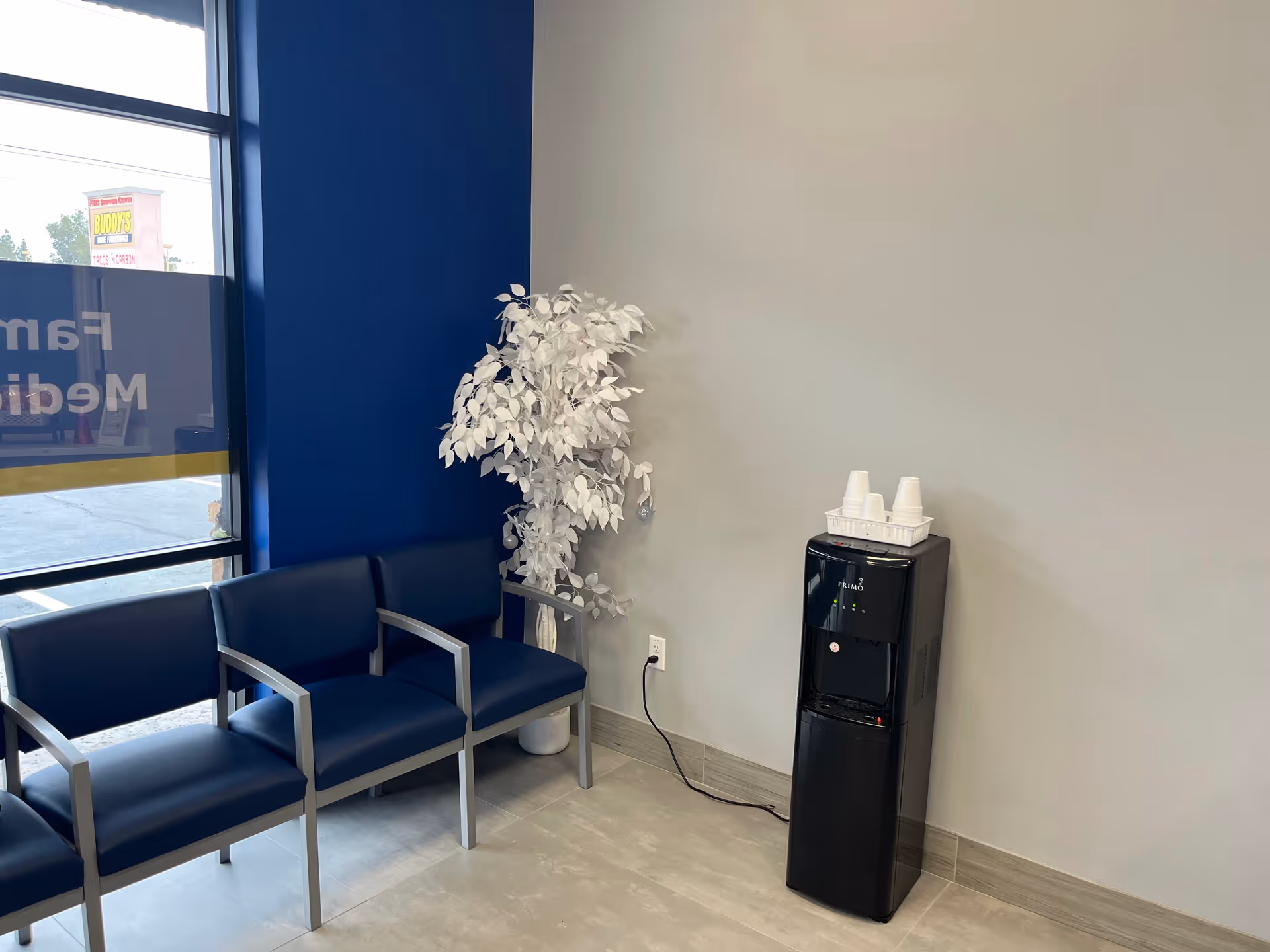 Interior waiting area with blue chairs, a water dispenser, and a white plant.
