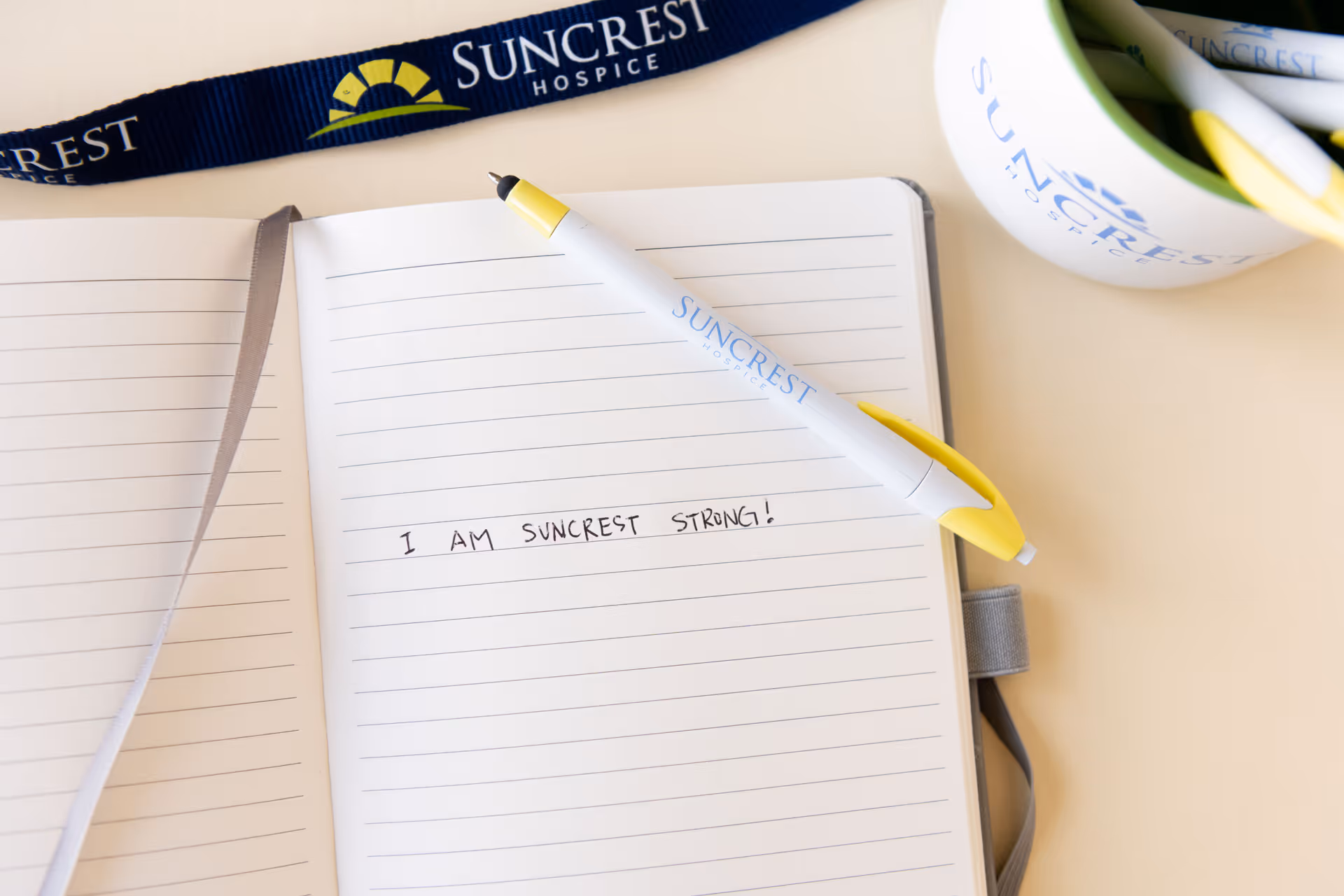 Notebook with SunCrest Hospice pen, mug, and lanyard arranged on a desk.