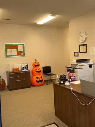Office reception area with Halloween pumpkins, bulletin board, printer, and wooden desk.